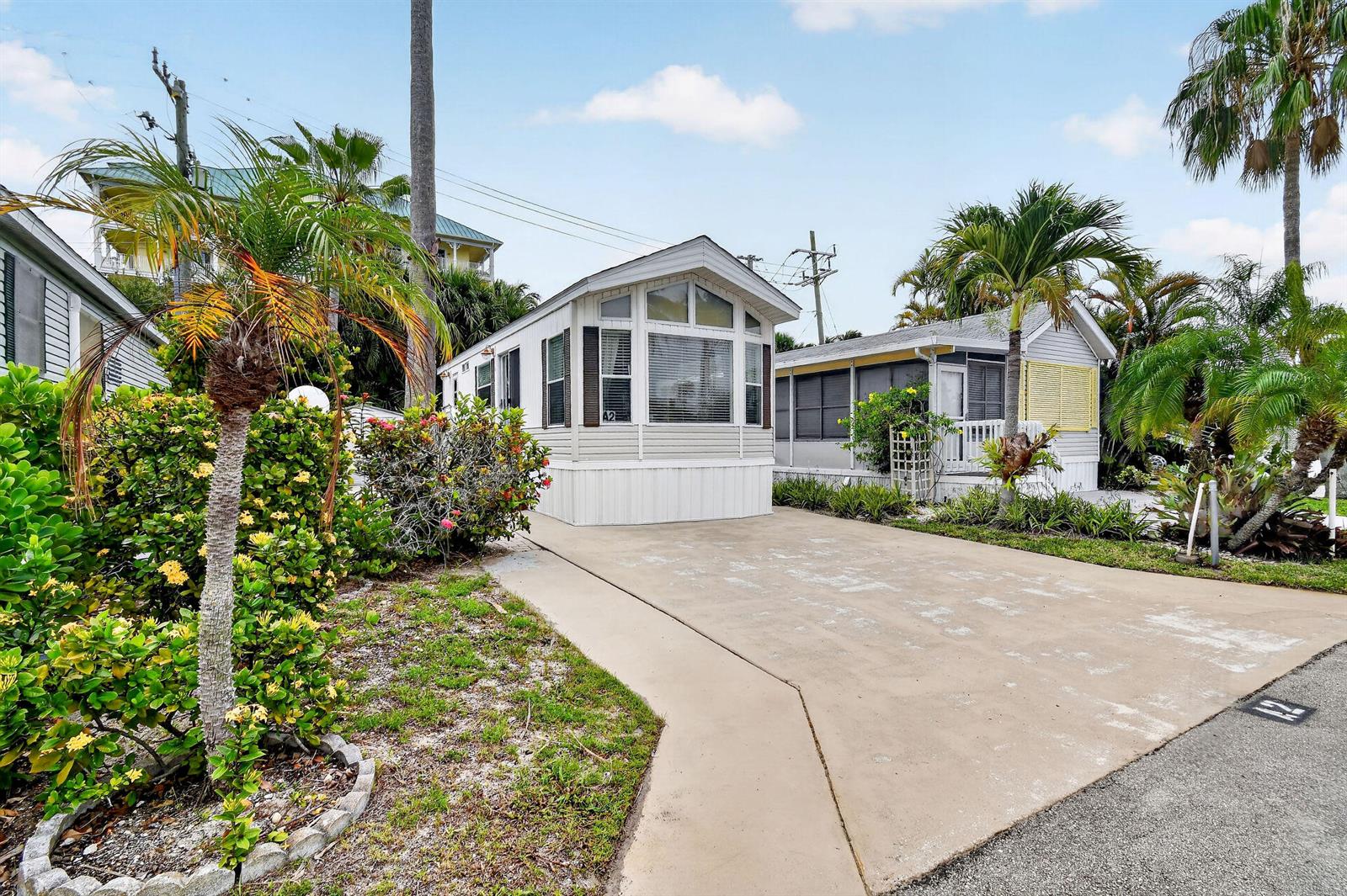A light-colored mobile home with a concrete driveway and palm trees in a sunny neighborhood — 900 Juno Ocean Walk # 2, Juno Beach FL 33408, JUNO BEACH, FL