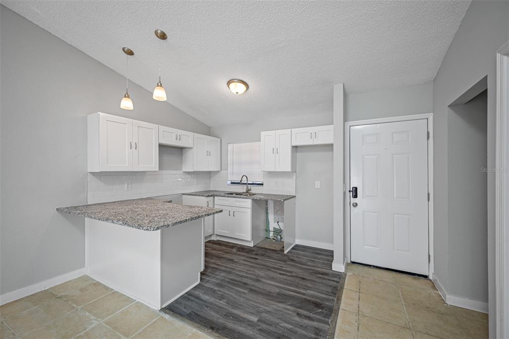 A kitchen with white cabinets, granite countertops, a tile backsplash, and mixed flooring — 501 ST. MICHAELS WAY UNIT 517, TARPON SPRINGS, FL