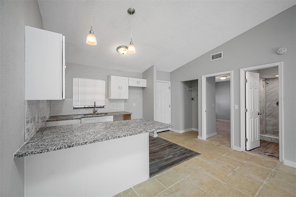 A kitchen with granite countertops, white cabinets, and tile flooring opens to a hallway — 501 ST. MICHAELS WAY UNIT 517, TARPON SPRINGS, FL