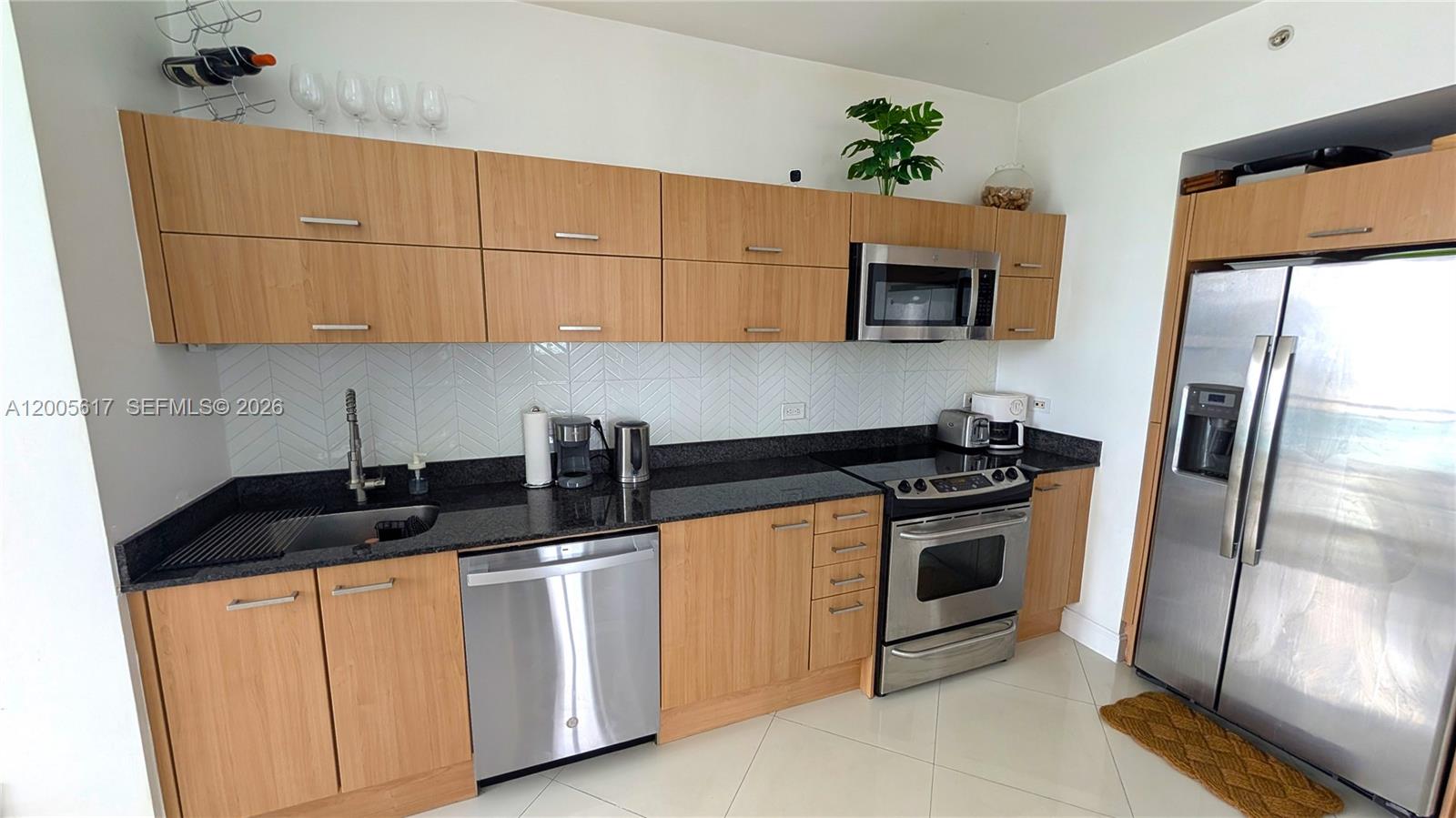 A kitchen features light wood cabinets, black granite countertops, stainless steel appliances, and herringbone backsplash — 350 S Miami Ave # 2813, Miami FL 33130, MIAMI, FL