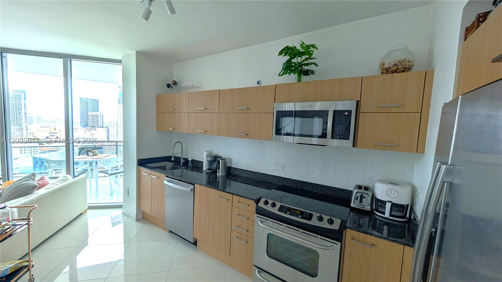 A modern kitchen features light wood cabinets, black granite countertops, and stainless steel appliances — 350 S Miami Ave # 2813, Miami FL 33130, MIAMI, FL