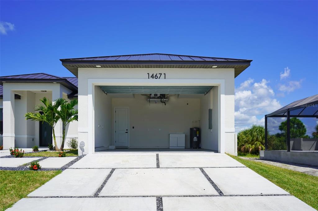 An open garage with a concrete driveway and a water heater inside — 14671 LILLIAN CIRCLE, PORT CHARLOTTE, FL