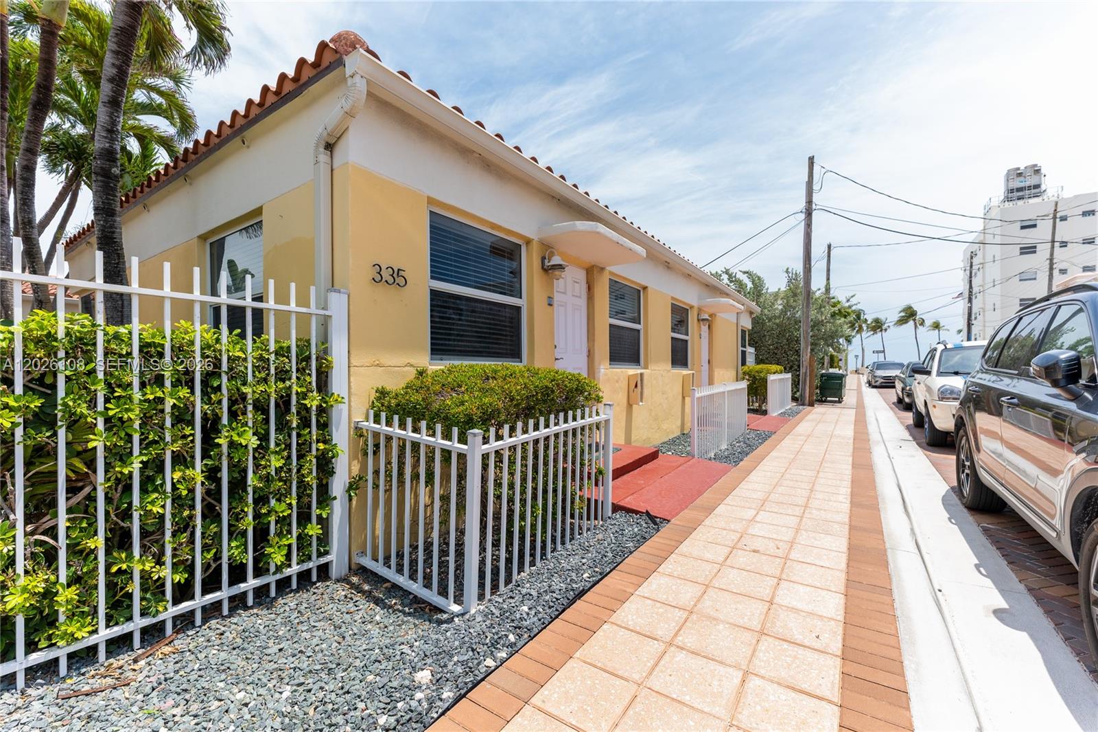 A yellow single-story building with a white fence sits beside a sidewalk and parked cars — 335 Georgia St, Hollywood FL 33019, HOLLYWOOD, FL