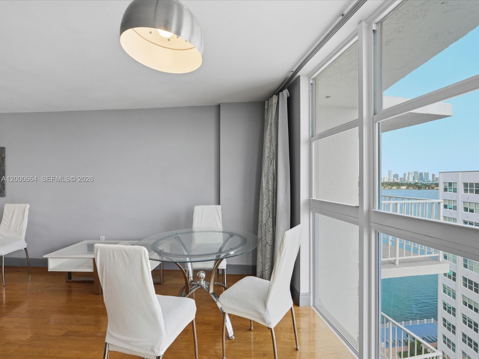 A dining area with a glass table, white chairs, and floor-to-ceiling windows overlooking water — 1228 West Ave # 1506, Miami Beach FL 33139, MIAMI BEACH, FL