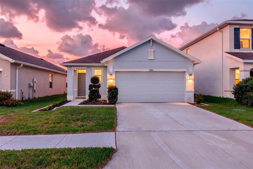 A light blue single-story house with a two-car garage under a pink sunset sky — 33801 JASMINE STAR LOOP, WESLEY CHAPEL, FL