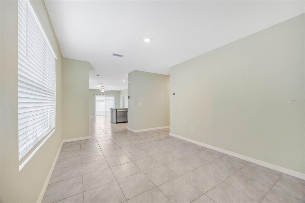 A room with light-colored tile flooring and a window with blinds leads to a kitchen — 33801 JASMINE STAR LOOP, WESLEY CHAPEL, FL