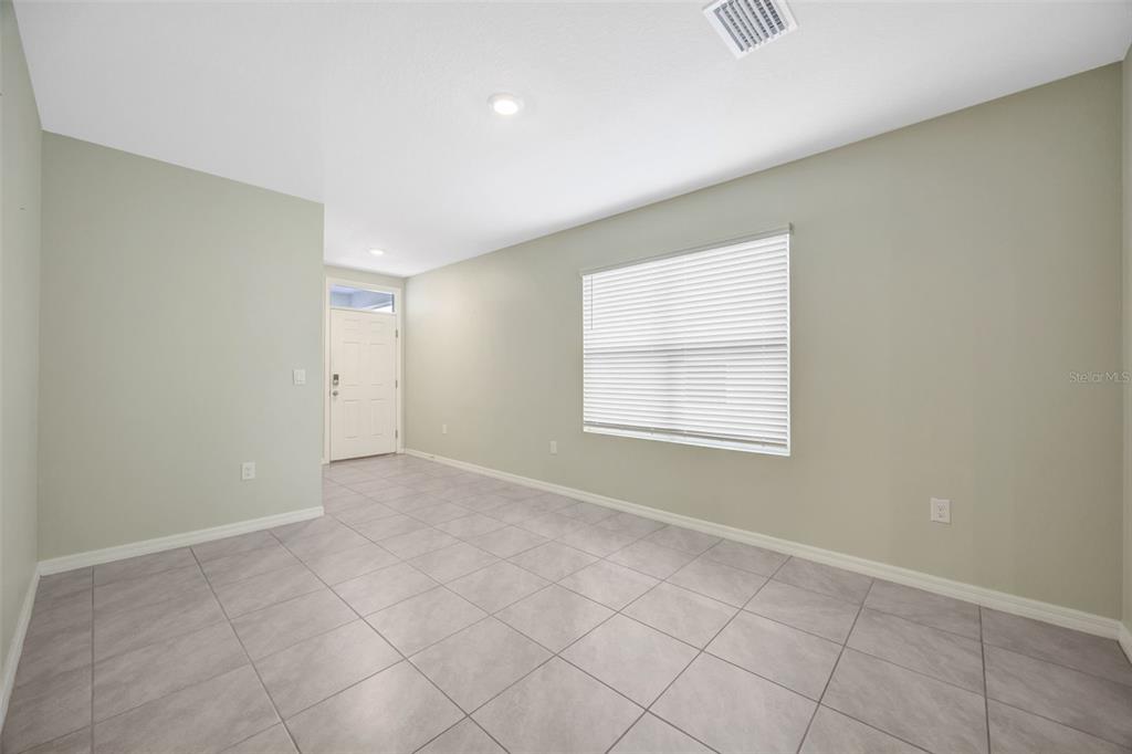 An empty room with light green walls, gray tile flooring, and a white front door — 33801 JASMINE STAR LOOP, WESLEY CHAPEL, FL