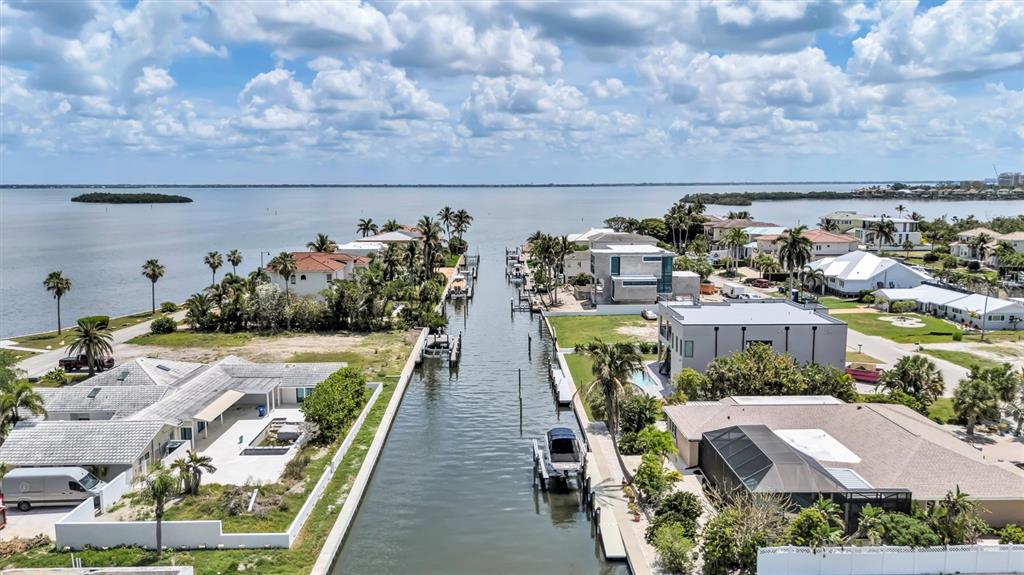 An aerial view shows waterfront homes lining a canal leading out to a large bay — 617 ROUNTREE DRIVE, LONGBOAT KEY, FL