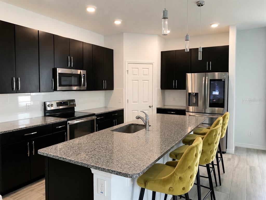 A kitchen features dark cabinets, granite countertops, a central island with bar seating, and appliances — 290 ABERDEEN STREET, DAVENPORT, FL