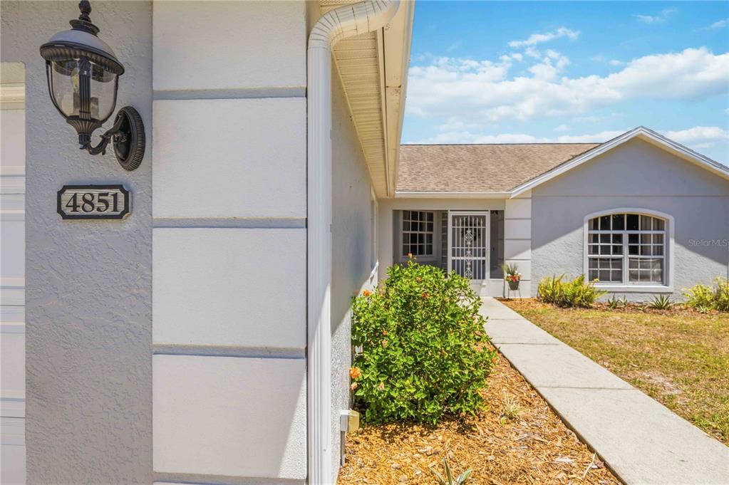A view of a house exterior featuring a walkway leading to a screened front entrance — 4851 HAMLETS GROVE DRIVE, SARASOTA, FL
