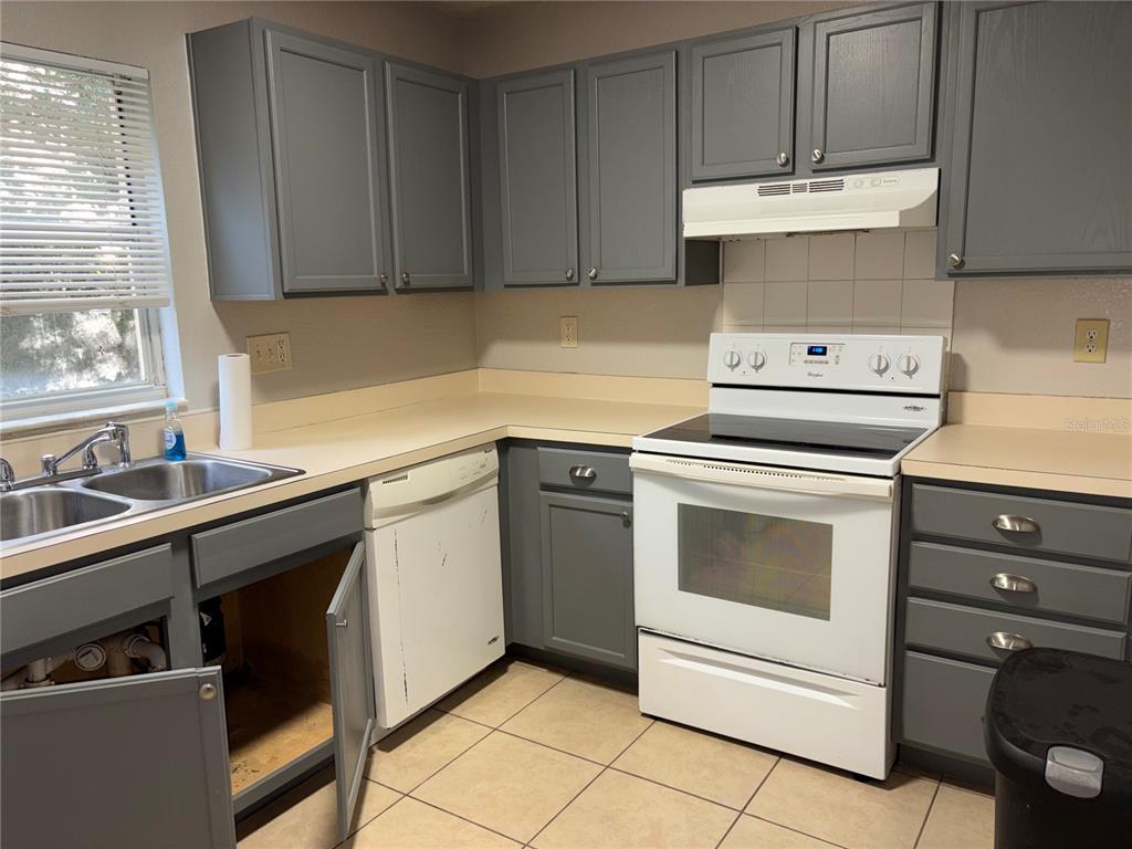 A kitchen features gray cabinets, white appliances, a double sink, and beige tile flooring — 5822 CONGRESS STREET UNIT 104, NEW PORT RICHEY, FL