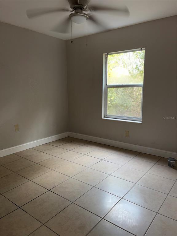 An empty bedroom features light-colored tile flooring, beige walls, and a ceiling fan — 5822 CONGRESS STREET UNIT 104, NEW PORT RICHEY, FL