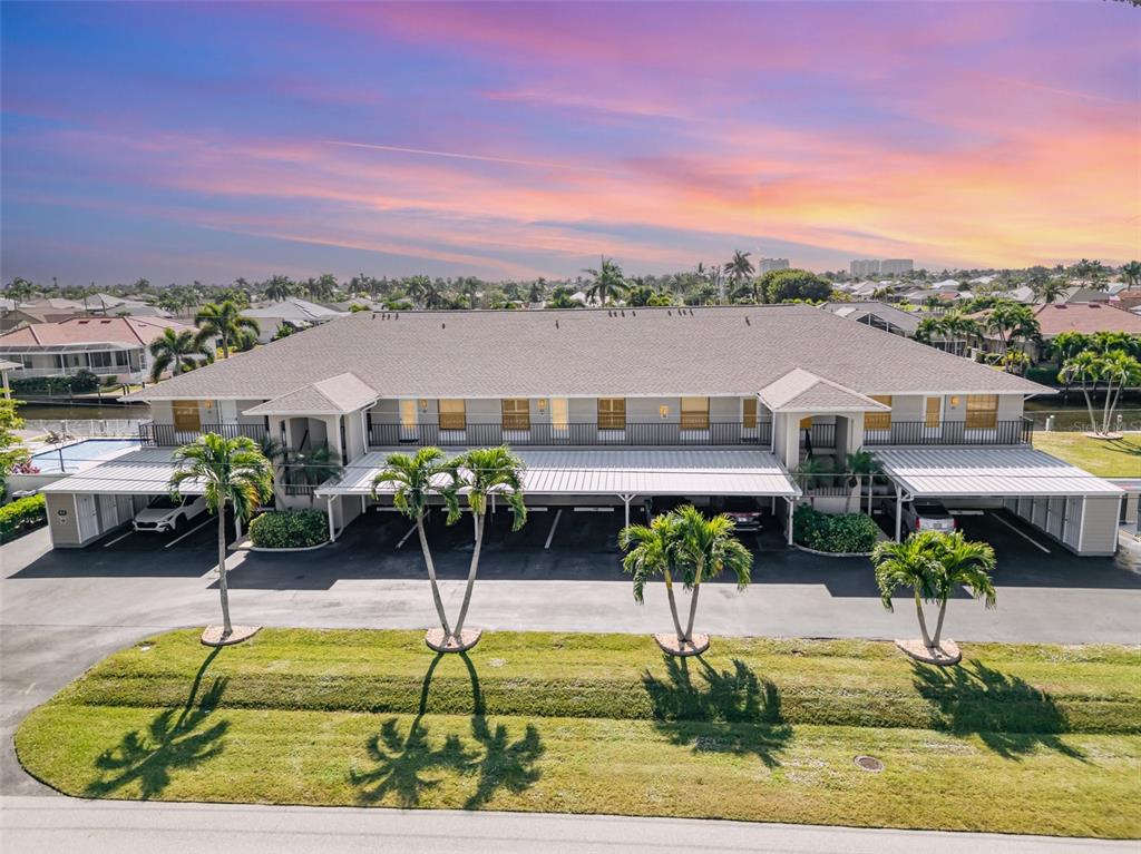 An exterior view of a two-story apartment building with covered parking and palm trees — 912 SW 48TH TERRACE UNIT 208, CAPE CORAL, FL
