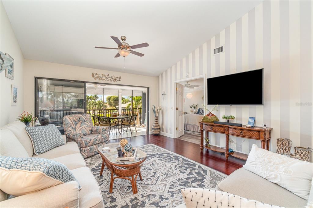 A living room features a striped accent wall, a mounted television, and a sliding glass door — 912 SW 48TH TERRACE UNIT 208, CAPE CORAL, FL