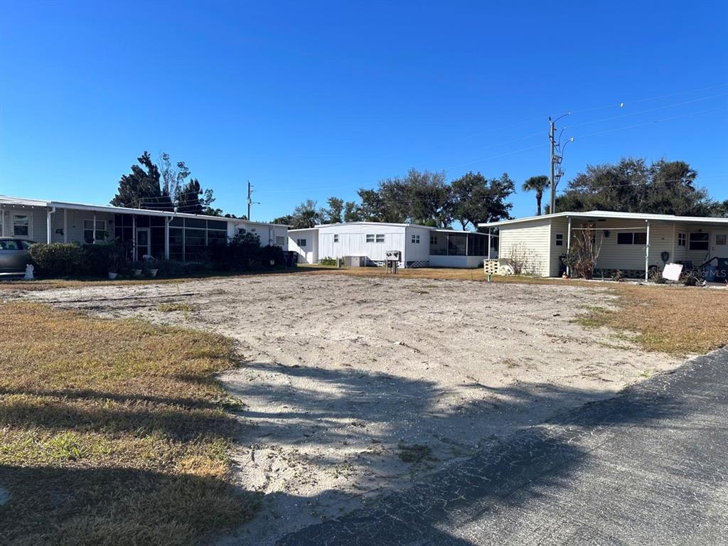 A vacant, sandy lot sits between two manufactured homes under a clear blue sky — 5302 CHATEAU LANE, BRADENTON, FL