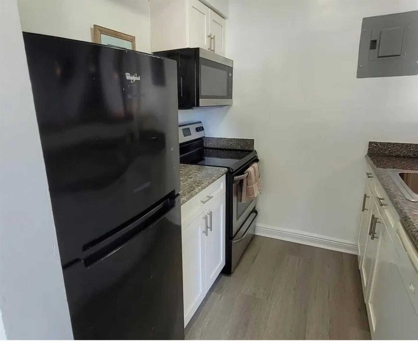 A small kitchen features white cabinets, granite countertops, and black appliances on wood-look flooring — 3226 NE 12th Street # 3, Pompano Beach FL 33062, POMPANO BEACH, FL