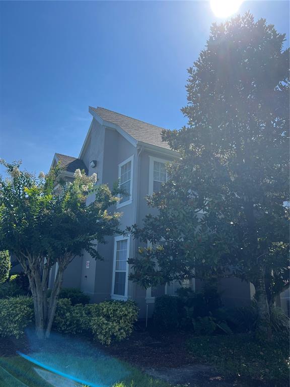 A two-story gray house exterior is partially obscured by a large tree and bushes — 9093 LEE VISTA BOULEVARD UNIT 903, ORLANDO, FL