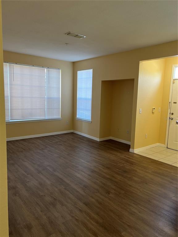An empty living room with wood-look flooring, beige walls, and two windows with blinds — 9093 LEE VISTA BOULEVARD UNIT 903, ORLANDO, FL