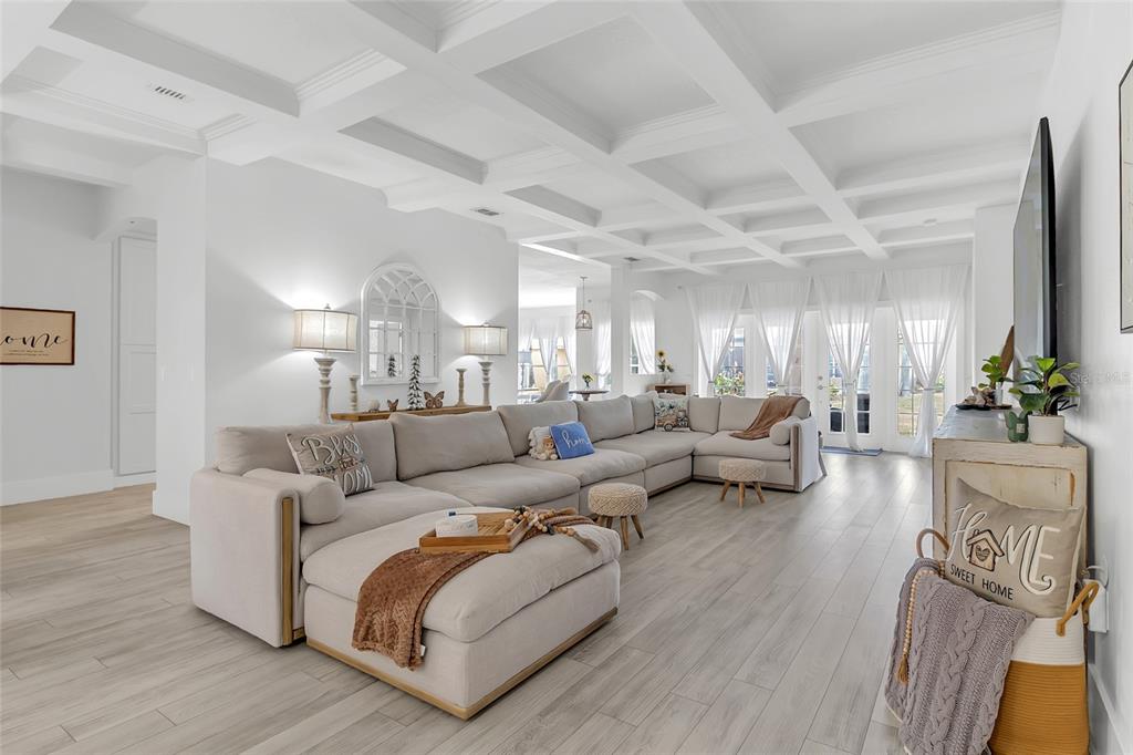 A bright living room features a large sectional sofa, coffered ceilings, and light wood flooring — 3609 VALLEYVIEW DRIVE, KISSIMMEE, FL