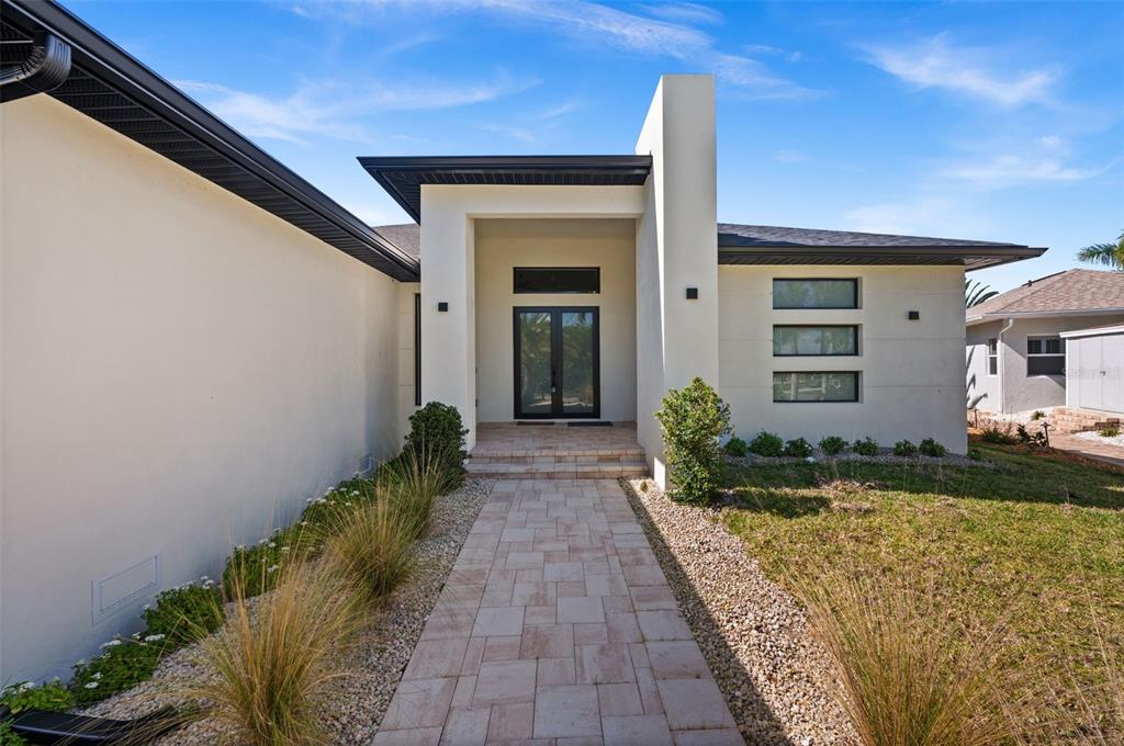 A paved walkway leads to the front entrance of a modern home with stucco siding — 10522 RIVERSIDE ROAD, PORT CHARLOTTE, FL