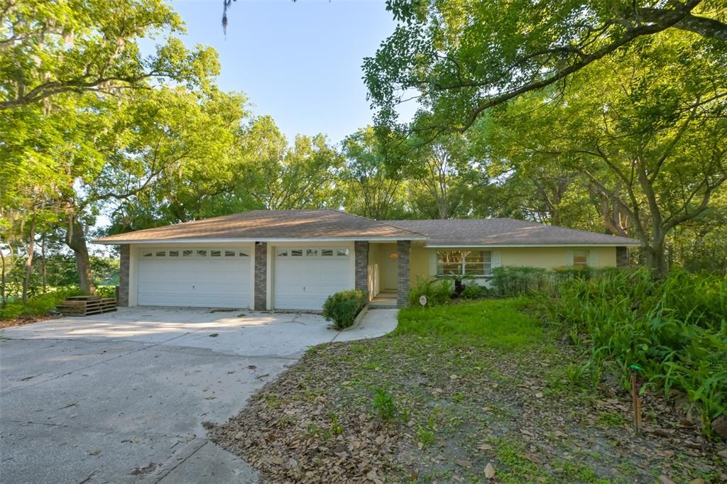 A single-story house with a two-car garage and a concrete driveway surrounded by trees — 36625 LAKE PASADENA ROAD, DADE CITY, FL