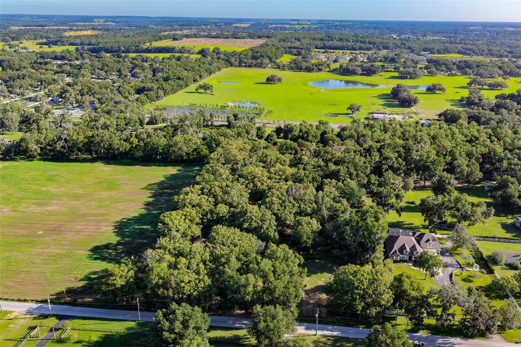 An aerial view shows a large house surrounded by dense trees and open green pastures — 36625 LAKE PASADENA ROAD, DADE CITY, FL
