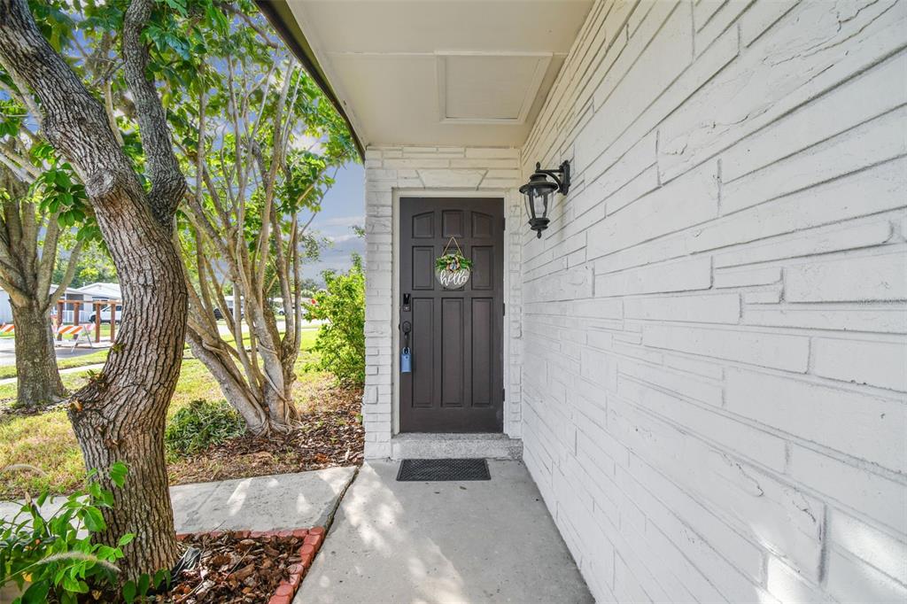 A dark brown front door with a hello sign sits under a covered porch — 6551 S WEST SHORE CIRCLE, TAMPA, FL