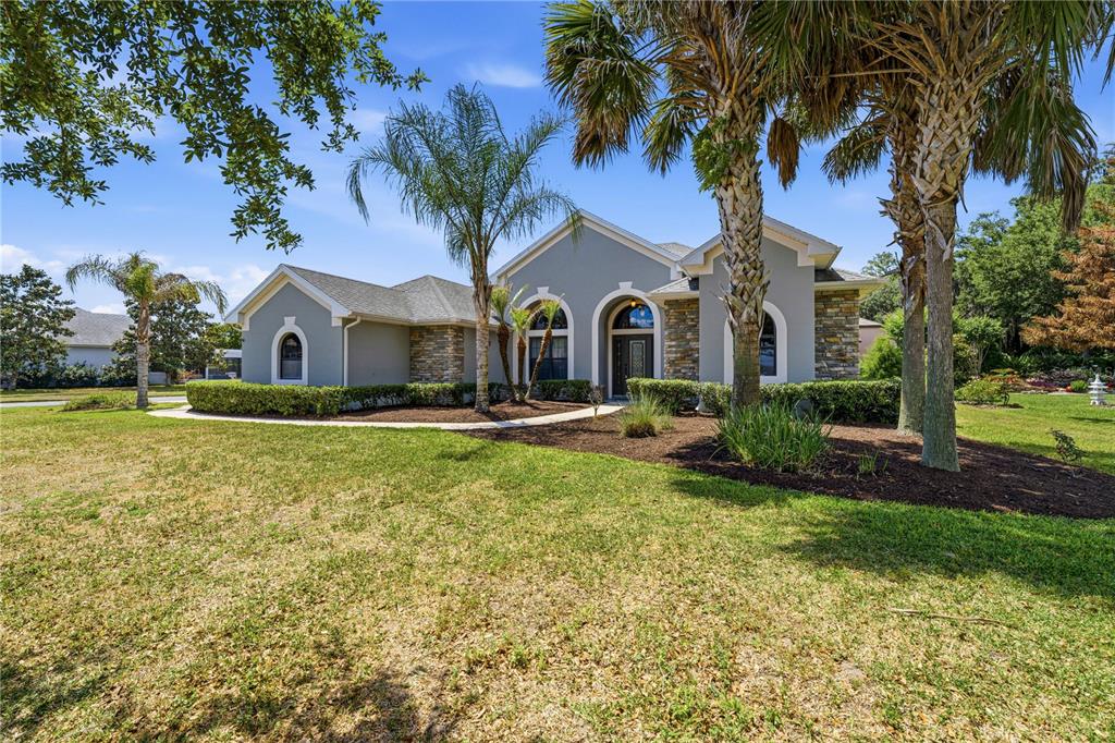 A single-story house with gray stucco, stone accents, and palm trees in the front yard — 8061 WATERBURY WAY, MOUNT DORA, FL