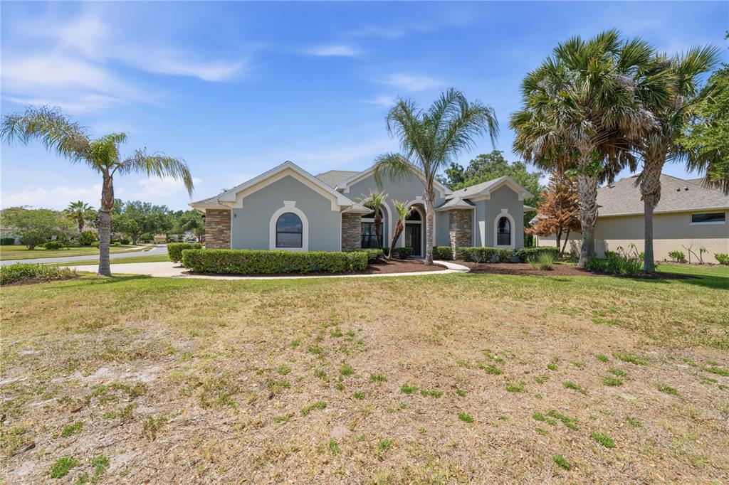 A single-story house with a light gray exterior, stone accents, and palm trees in the yard — 8061 WATERBURY WAY, MOUNT DORA, FL