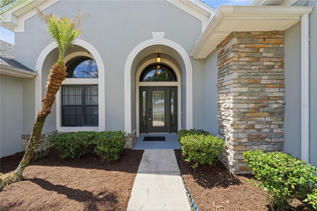 The front exterior of a house features a stone pillar, arched entryway, and a palm tree — 8061 WATERBURY WAY, MOUNT DORA, FL