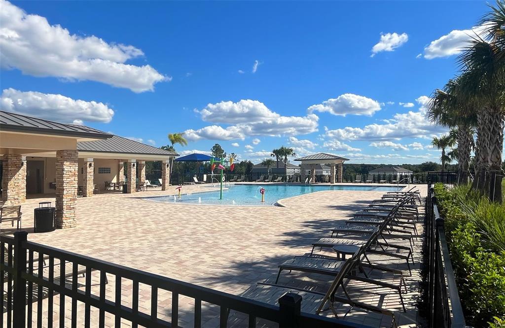 A swimming pool with a splash pad sits on a paved patio with lounge chairs — 6888 SPANISH IMPERIAL STREET, HOWEY IN THE HILLS, FL