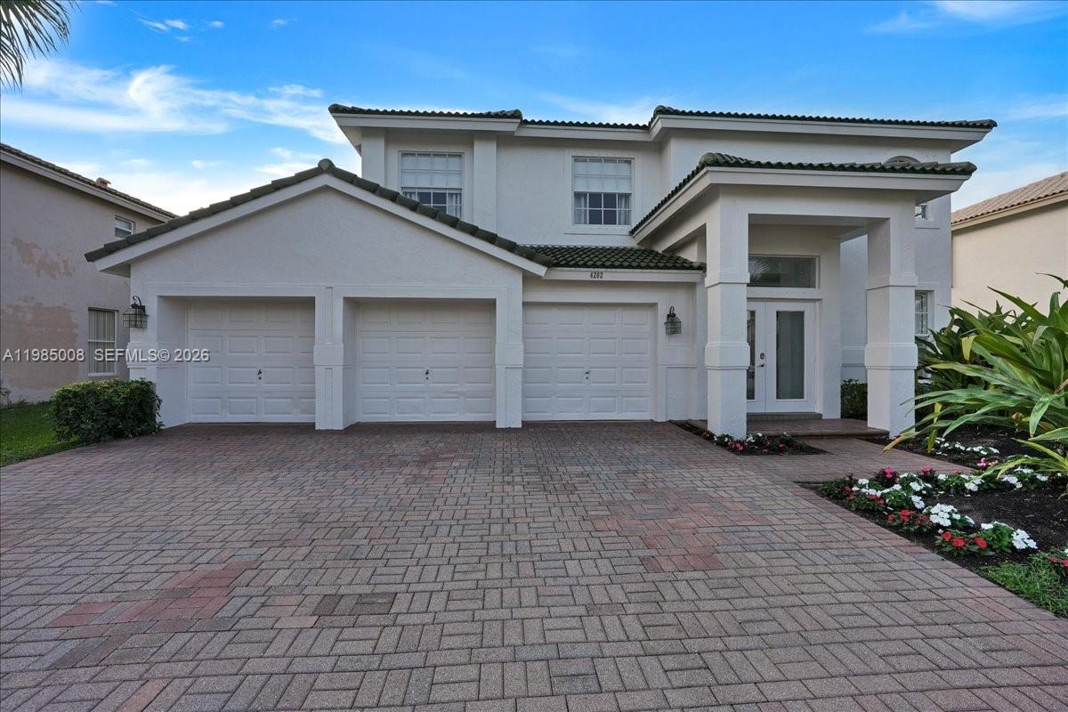 A two-story house features a three-car garage and a paved driveway under a blue sky — 4202 Bahia Isle Cir, Wellington FL 33449, WELLINGTON, FL
