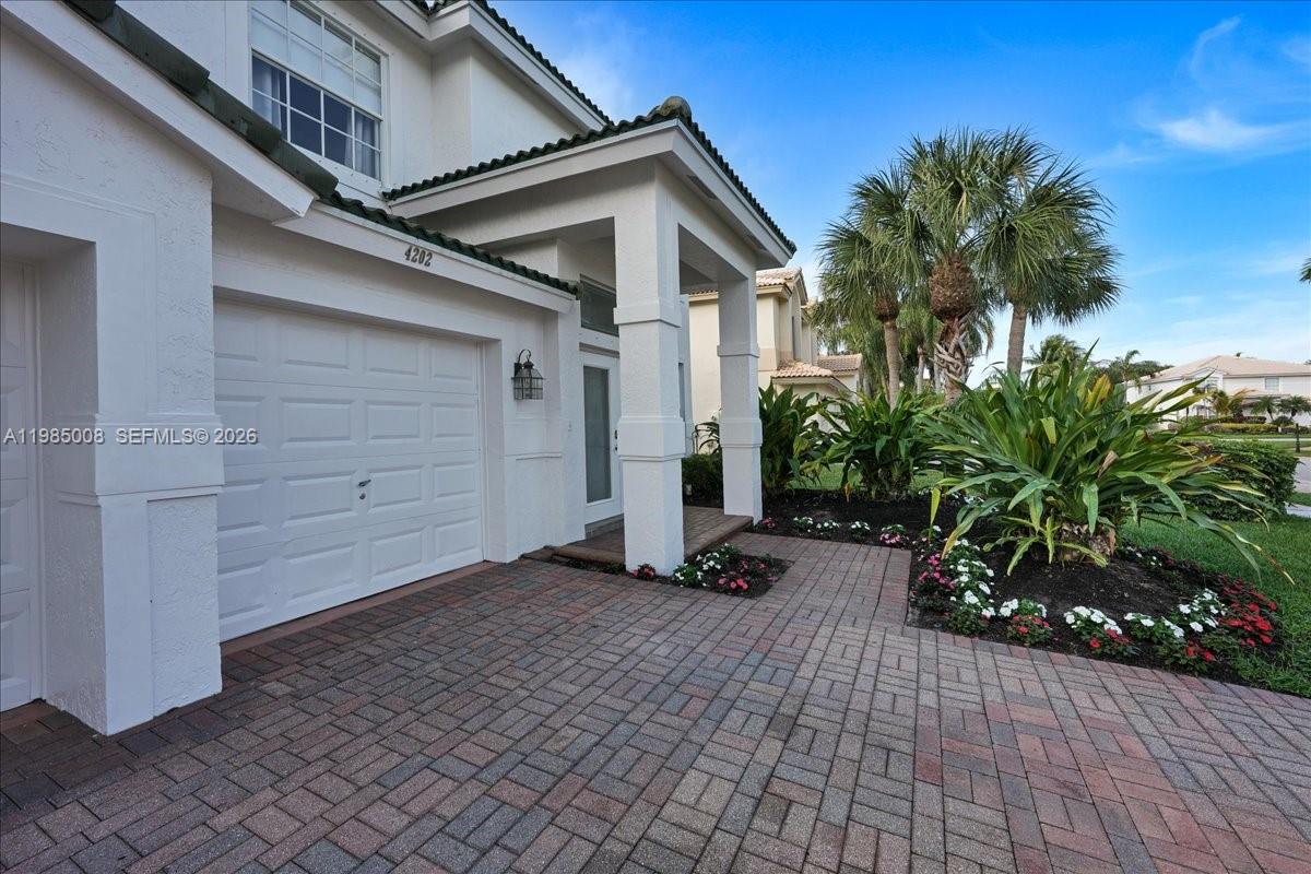 A paved driveway leads to a white garage and a covered entryway with landscaping — 4202 Bahia Isle Cir, Wellington FL 33449, WELLINGTON, FL