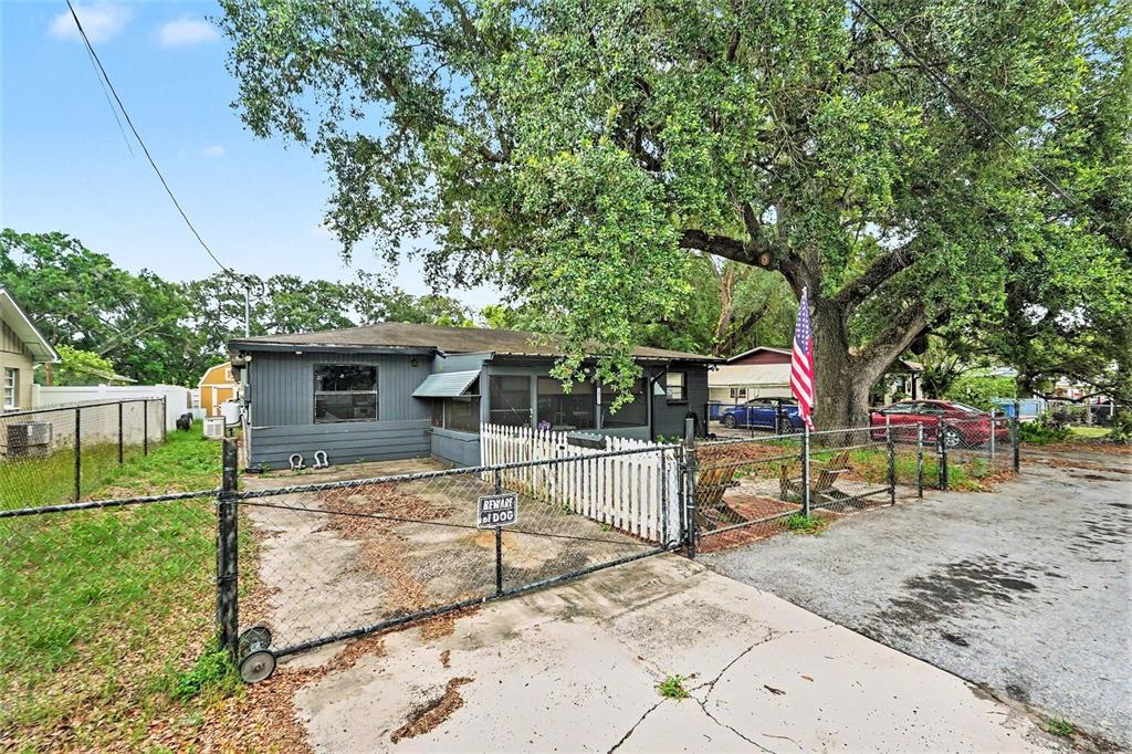 A gray house with a fenced yard, a large oak tree, and an American flag — 14925 FISHER ROAD, TAMPA, FL