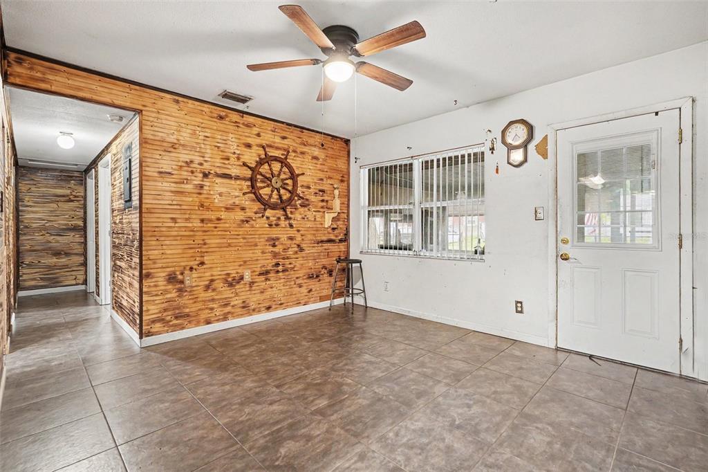 A room with tile flooring, a wood-paneled accent wall, a ceiling fan, and a door — 14925 FISHER ROAD, TAMPA, FL