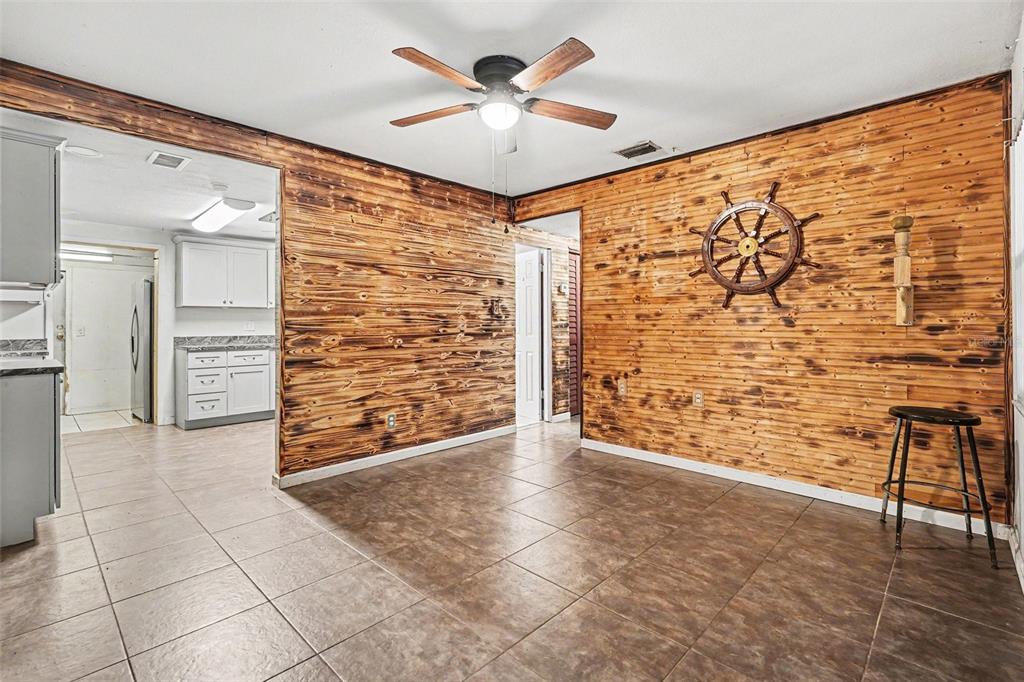 A dining room with wood-paneled walls, tile flooring, a ceiling fan, and a ship wheel — 14925 FISHER ROAD, TAMPA, FL