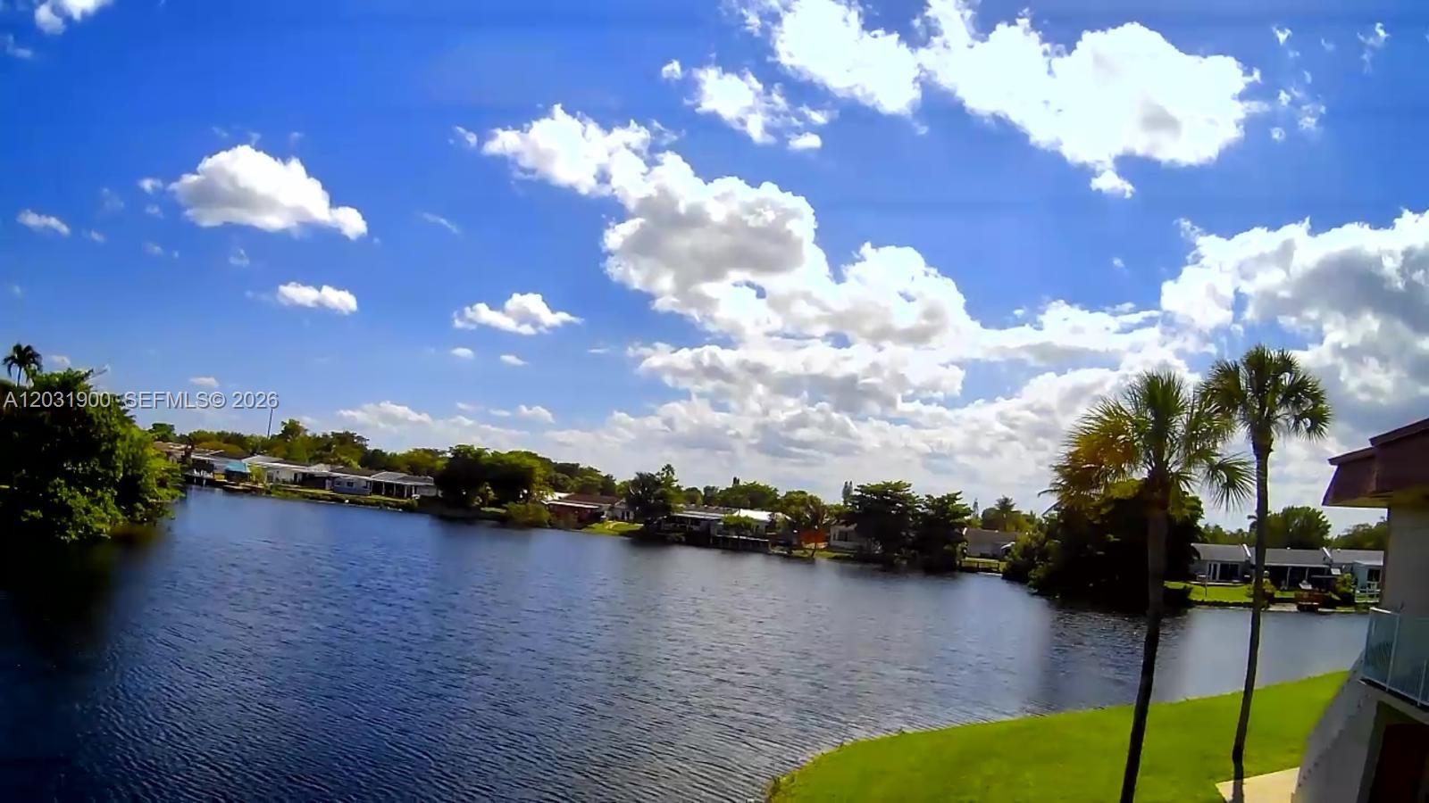 A grassy lawn slopes down to a lake with palm trees and distant houses — 12860 SW 43rd Dr # B, Miami FL 33175, MIAMI, FL