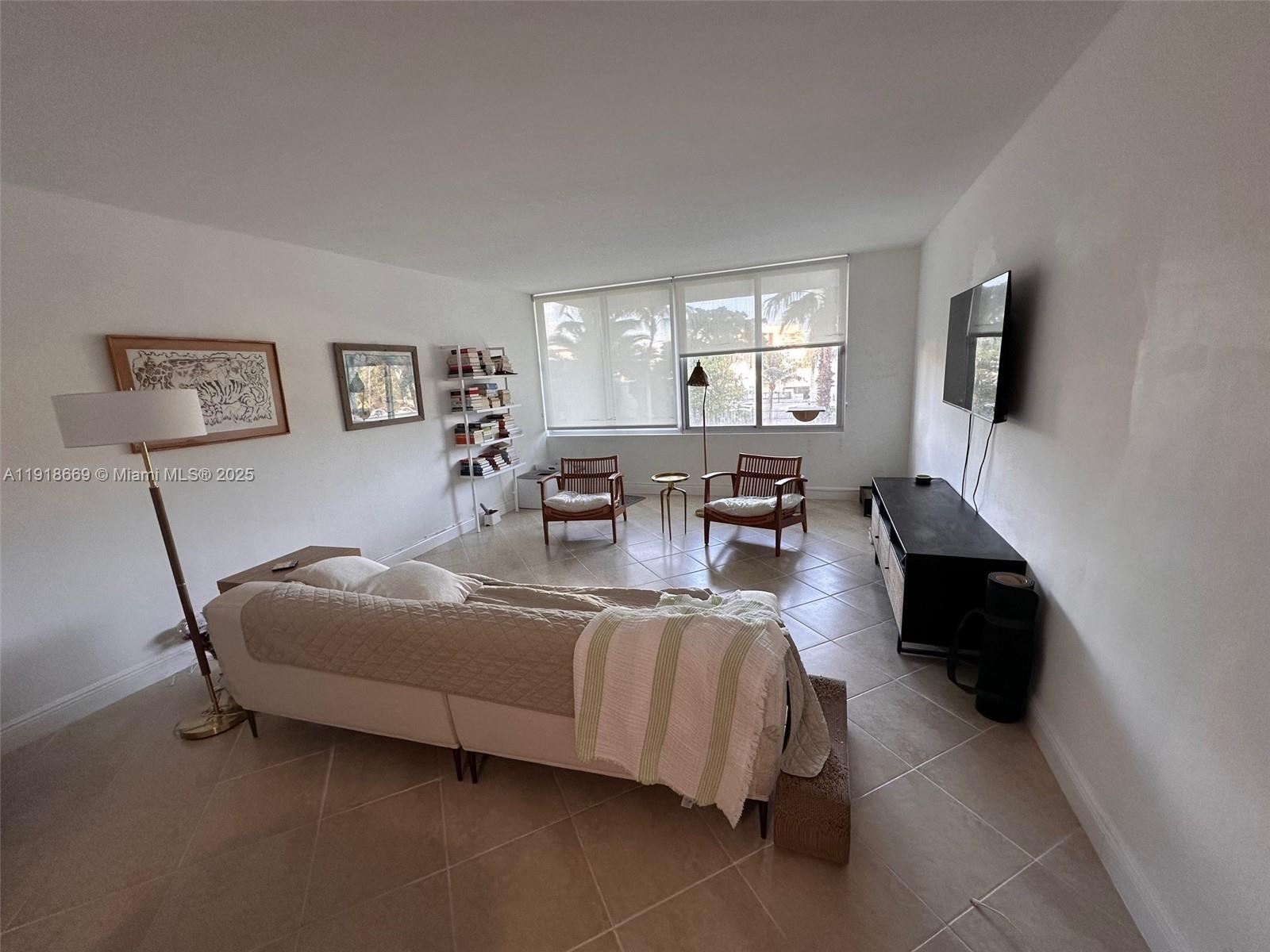 A living room features a sofa, two wooden chairs, a bookshelf, and a wall-mounted television — 1000 West Ave # 225, Miami Beach FL 33139, MIAMI BEACH, FL