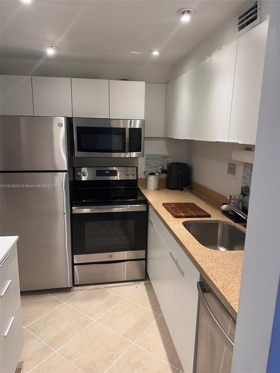 A galley kitchen features stainless steel appliances, white cabinetry, and tan speckled countertops — 1000 West Ave # 225, Miami Beach FL 33139, MIAMI BEACH, FL