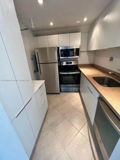 A galley kitchen features white cabinets, stainless steel appliances, and light-colored tile flooring — 1000 West Ave # 225, Miami Beach FL 33139, MIAMI BEACH, FL