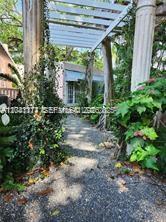 A gravel path leads through a white pergola toward a small house surrounded by greenery — 3940 Main, Miami FL 33133, MIAMI, FL