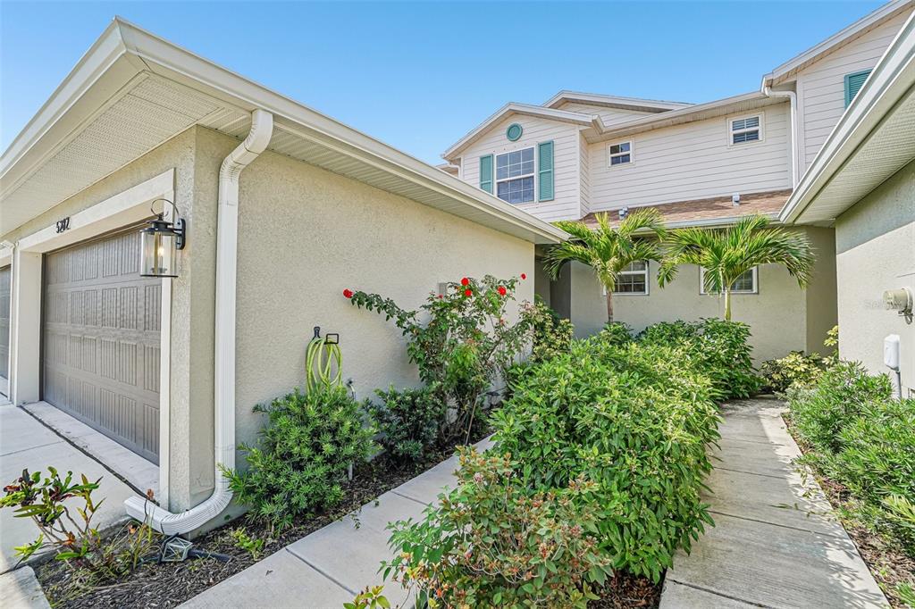 A beige two-story house exterior features a garage, a walkway, and lush green landscaping — 5282 NEIL DRIVE, ST PETERSBURG, FL