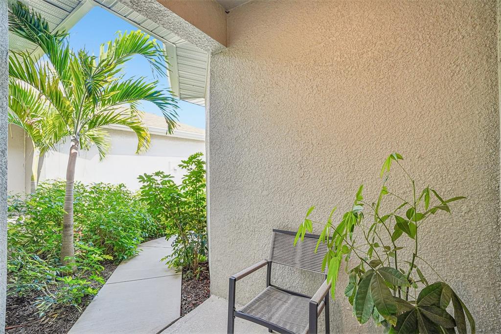 A covered outdoor patio features a textured beige wall, a chair, and surrounding tropical landscaping — 5282 NEIL DRIVE, ST PETERSBURG, FL