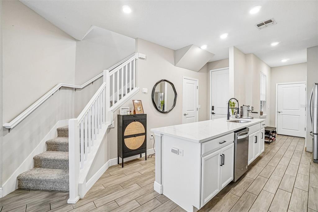 A kitchen with a white island, stainless steel dishwasher, and stairs with a white railing — 5282 NEIL DRIVE, ST PETERSBURG, FL