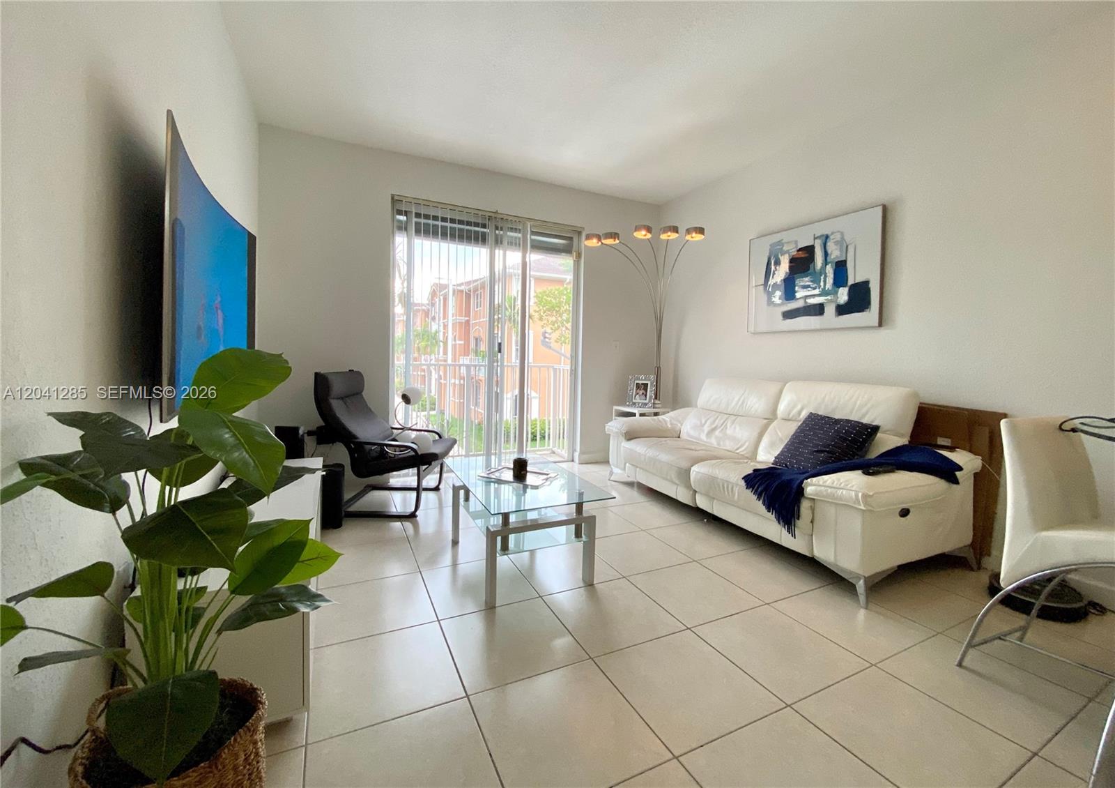 A living room features a white sofa, glass coffee table, tile flooring, and a balcony view — 7250 NW 177th St # 16, Hialeah FL 33015, HIALEAH, FL