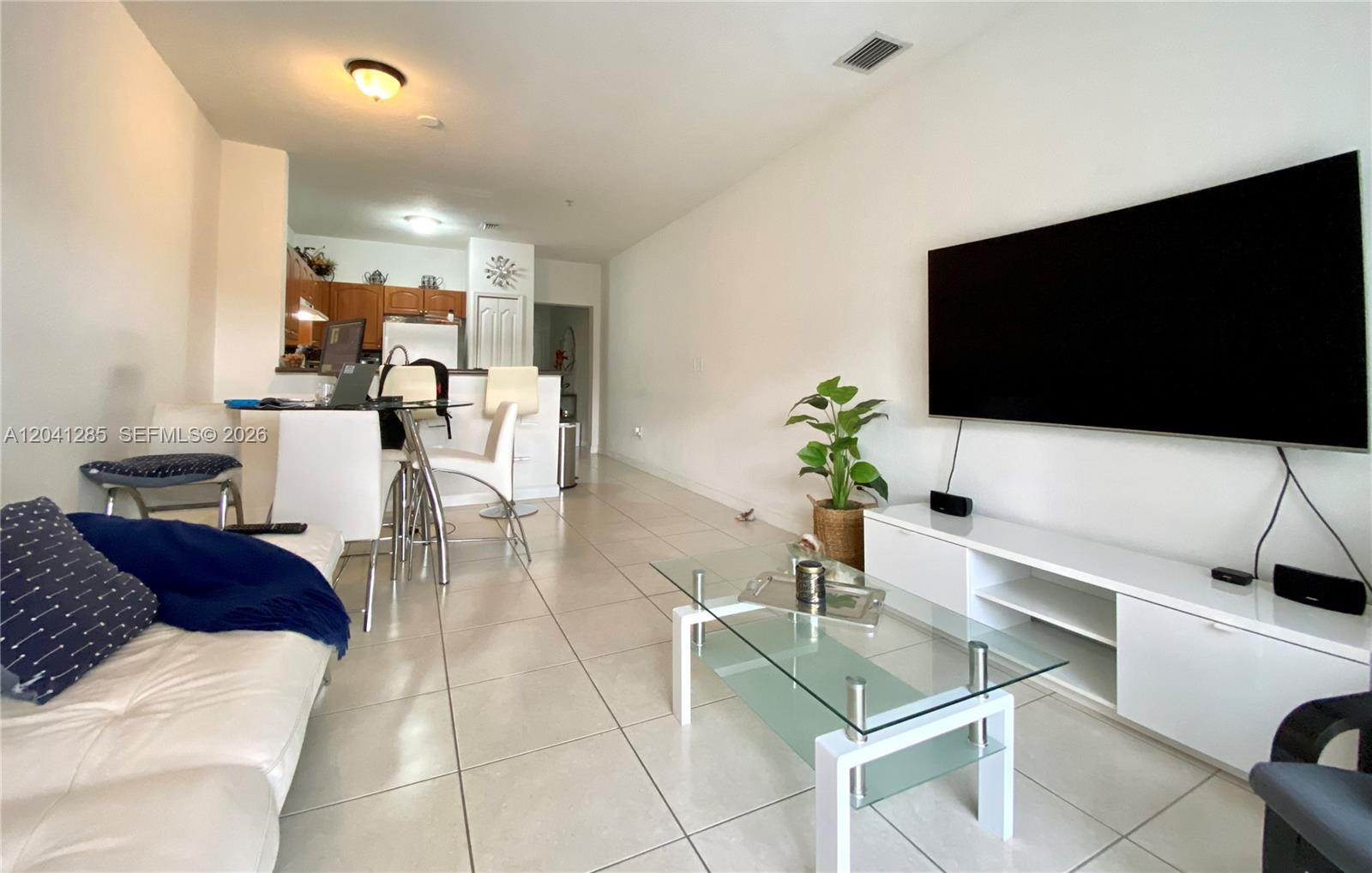 A living room with tile floors, a glass coffee table, and a wall-mounted television — 7250 NW 177th St # 16, Hialeah FL 33015, HIALEAH, FL