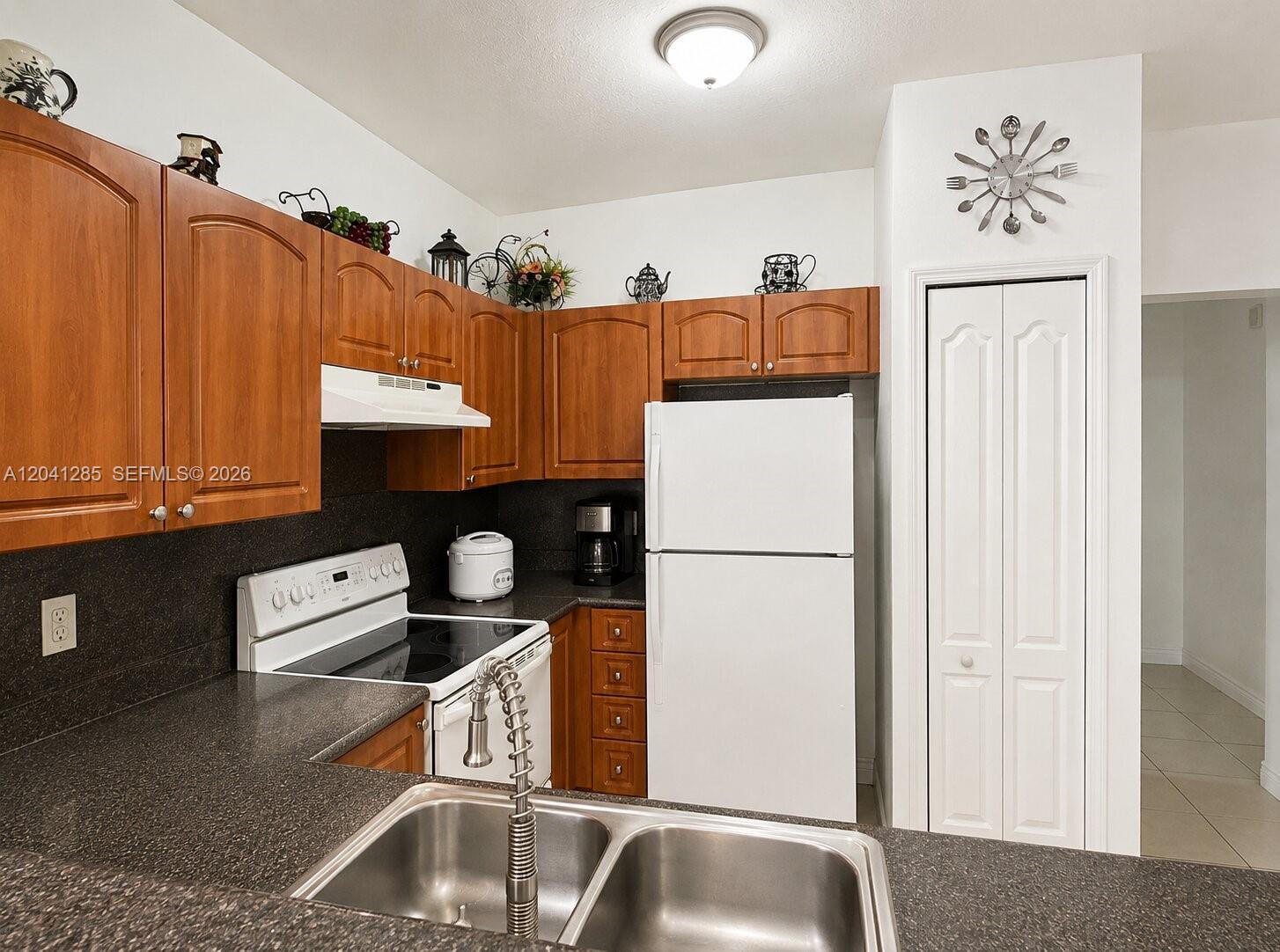This kitchen features wood cabinets, dark countertops, a white refrigerator, and a stainless steel sink — 7250 NW 177th St # 16, Hialeah FL 33015, HIALEAH, FL
