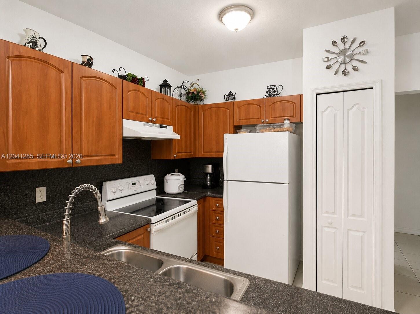 A kitchen features wood cabinets, white appliances, dark countertops, and a double sink — 7250 NW 177th St # 16, Hialeah FL 33015, HIALEAH, FL
