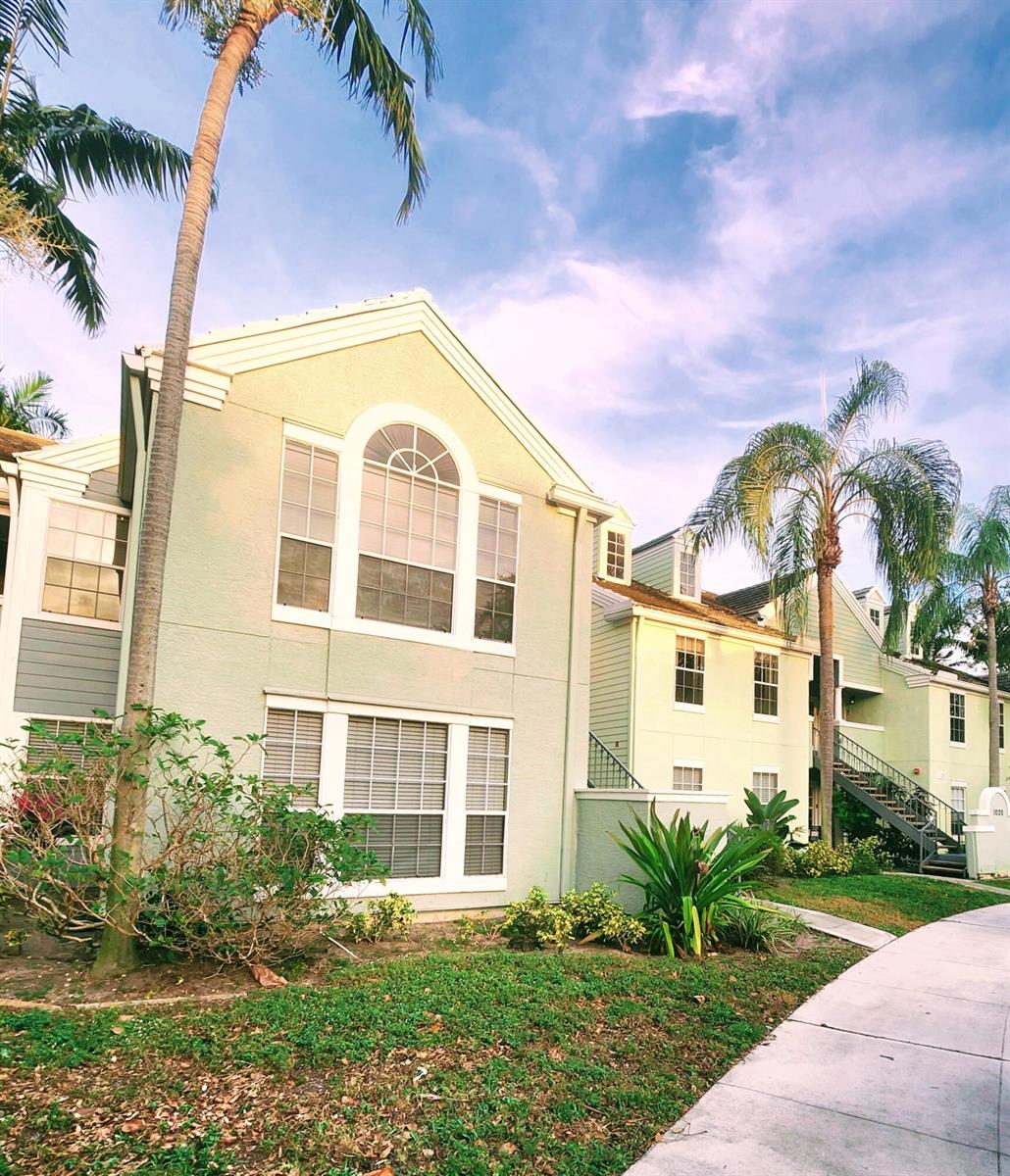 Exterior view of a multi-story apartment building with light-colored siding and palm trees — 1020 Crystal Way # C, Delray Beach FL 33444, DELRAY BEACH, FL