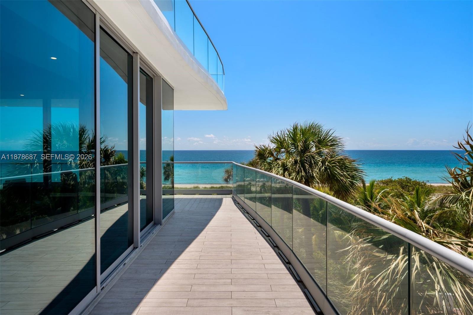 A modern balcony with glass railings overlooks the ocean and palm trees — 9349 Collins Ave # 406, Surfside FL 33154, SURFSIDE, FL